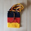 Handgehäkelte Umhängetasche in den Farben Schwarz, Rot und Gold, inspiriert von der deutschen Flagge. Mit breitem, verstellbarem Schultergurt, stabilem Kordelzugverschluss und dekorativem Kordelende. Etwa 19 x 26 cm groß, bietet Platz für Alltagsutensilien wie Handy, Geldbörse und Schlüssel. Stilvolles, handgemachtes Accessoire für Fans und Liebhaber deutscher Farben.