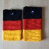 Handgehäkelte Handyhülle in den Farben Schwarz, Rot und Gold, angeordnet wie die deutsche Flagge. Aus robustem Baumwollgarn gefertigt, mit weicher Struktur und sicherem Knopfverschluss oben. Schützt das Smartphone vor Kratzern und Stößen. Erhältlich in zwei Größen – ein handgemachtes Accessoire für Fans und Liebhaber deutscher Farben.