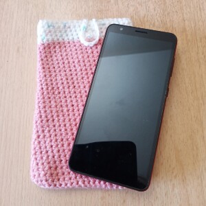 Handgehäkelte zweifarbige Handyhülle Rosa-Weiß aus weicher, strapazierfähiger Wolle mit dekorativem Knopfverschluss. Die Hülle misst etwa 10 x 16 cm, ist dehnbar und passt sich der Form des Smartphones an. In sanften Pastelltönen gestaltet, schützt sie das Handy vor Kratzern und Stößen – ein stilvolles, handgefertigtes Accessoire mit liebevollen Details.