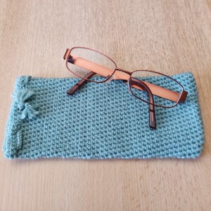 Handgehäkeltes Brillenetui Mintgrün aus weicher Baumwolle mit handgeflochtenem Kordelzug. Das etwa 9 x 20 cm große Etui bietet Platz für Lese-, Sonnen- oder Sehbrillen und schützt sie zuverlässig vor Kratzern und leichten Stößen. Leichtes, schlankes Design mit rustikalem Charme – in verschiedenen Farben erhältlich, handgefertigt und nachhaltig hergestellt.
