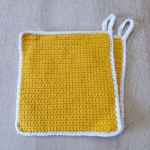 Handgehäkeltes Topflappen-Set Gelb-Weiß aus robustem Baumwollgarn, quadratisch mit ca. 16 x 16 cm Größe. Die gleichmäßige Häkelstruktur sorgt für Hitzeschutz beim Kochen und Backen. Jeder Topflappen hat eine stabile Aufhängeschlaufe und ist wahlweise einfarbig oder mit farbigem Rand gestaltet – ein dekorativer, funktionaler Küchenhelfer in Handarbeit.