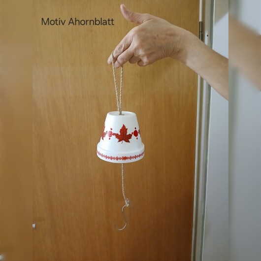 Handbemalte Futterglocke Motiv Ahornblatt aus einem Tontopf, bunt verziert mit Serviettentechnik, hängt an einer dicken Kordel. Im Inneren ist ein Metallhaken für Vogelfutter angebracht. Dekorative Winterfütterung für kleine Gartenvögel.