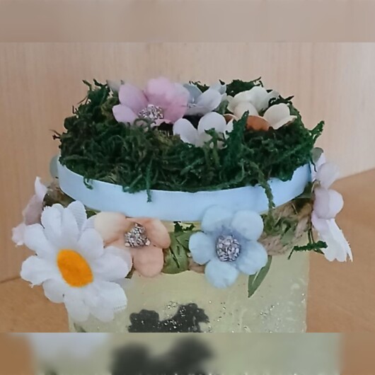 Handgefertigtes Feenglas mit romantischem Feenmotiv, verziert mit blauem Satinband, feinem Glitzerstaub und einer kleinen Mooslandschaft auf dem Deckel. Umgeben von zarten Kunstblumen wirkt das Glas wie ein leuchtender Miniaturgarten. Im Inneren sorgt ein flackerndes LED-Teelicht für warmes, magisches Licht – ein märchenhaftes Deko- und Nachtlicht für jeden Raum.