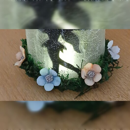 Handgefertigtes Feenglas mit romantischem Feenmotiv, verziert mit blauem Satinband, feinem Glitzerstaub und einer kleinen Mooslandschaft auf dem Deckel. Umgeben von zarten Kunstblumen wirkt das Glas wie ein leuchtender Miniaturgarten. Im Inneren sorgt ein flackerndes LED-Teelicht für warmes, magisches Licht – ein märchenhaftes Deko- und Nachtlicht für jeden Raum.