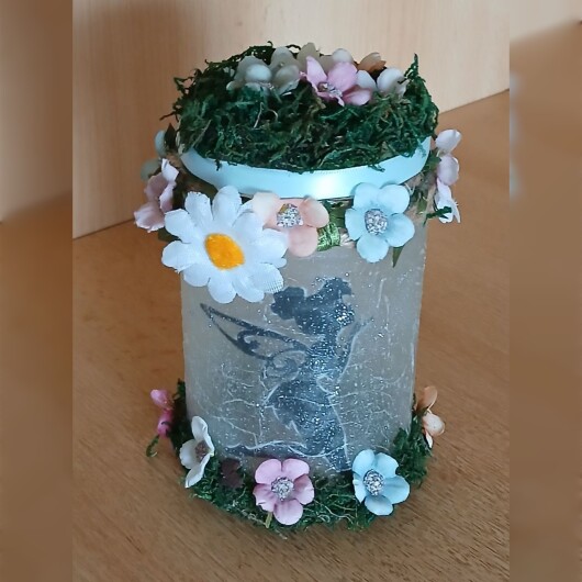 Handgefertigtes Feenglas Fee Motiv 3 mit romantischem Feenmotiv, verziert mit blauem Satinband, feinem Glitzerstaub und einer kleinen Mooslandschaft auf dem Deckel. Umgeben von zarten Kunstblumen wirkt das Glas wie ein leuchtender Miniaturgarten. Im Inneren sorgt ein flackerndes LED-Teelicht für warmes, magisches Licht – ein märchenhaftes Deko- und Nachtlicht für jeden Raum.