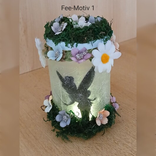 Handgefertigtes Feenglas Fee Motiv 1 mit romantischem Feenmotiv, verziert mit blauem Satinband, feinem Glitzerstaub und einer kleinen Mooslandschaft auf dem Deckel. Umgeben von zarten Kunstblumen wirkt das Glas wie ein leuchtender Miniaturgarten. Im Inneren sorgt ein flackerndes LED-Teelicht für warmes, magisches Licht – ein märchenhaftes Deko- und Nachtlicht für jeden Raum.