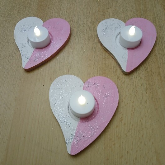 Handbemalte Herz Teelichthalter Rosa-Weiß aus Holz im 4er Set, jeweils mit farbenfrohen, individuellen Designs. In der Mitte jedes Herzens befindet sich eine Vertiefung für ein kleines Teelicht, das warmes Licht auf das bemalte Holz wirft. Das 4er-Set strahlt Gemütlichkeit und Liebe aus – perfekt als romantische Deko, Geschenk oder Lichtakzent für Valentinstag, Hochzeit oder Alltag.