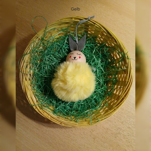 Handgefertigte Pompon-Osterhäschen Gelb aus weichem, flauschigem Material in fröhlichen Farben wie Rosa, Gelb, Hellblau, Weiß und Dunkelgrün. Jedes Häschen hat lange graue Filzohren, handbemalte Augen, Nase und rosige Wangen sowie eine graue Aufhängeschlaufe. Die niedlichen Anhänger verbreiten frühlingshafte Osterstimmung an Zweigen, Fenstern oder Geschenken.