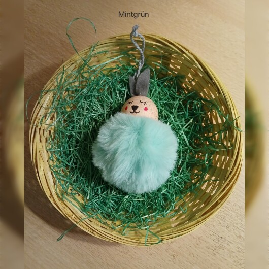 Handgefertigte Pompon-Osterhäschen Mintgrün aus weichem, flauschigem Material in fröhlichen Farben wie Rosa, Gelb, Hellblau, Weiß und Dunkelgrün. Jedes Häschen hat lange graue Filzohren, handbemalte Augen, Nase und rosige Wangen sowie eine graue Aufhängeschlaufe. Die niedlichen Anhänger verbreiten frühlingshafte Osterstimmung an Zweigen, Fenstern oder Geschenken.