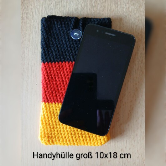 Handgehäkelte Handyhülle groß 10x18 cm in den Farben Schwarz, Rot und Gold, angeordnet wie die deutsche Flagge. Aus robustem Baumwollgarn gefertigt, mit weicher Struktur und sicherem Knopfverschluss oben. Schützt das Smartphone vor Kratzern und Stößen. Ein handgemachtes Accessoire für Fans und Liebhaber deutscher Farben.