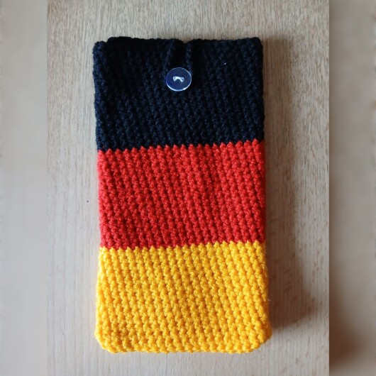 Handgehäkelte Handyhülle groß 10x18 cm in den Farben Schwarz, Rot und Gold, angeordnet wie die deutsche Flagge. Aus robustem Baumwollgarn gefertigt, mit weicher Struktur und sicherem Knopfverschluss oben. Schützt das Smartphone vor Kratzern und Stößen. Ein handgemachtes Accessoire für Fans und Liebhaber deutscher Farben.