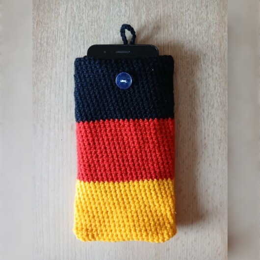 Handgehäkelte Handyhülle groß 10x18 cm in den Farben Schwarz, Rot und Gold, angeordnet wie die deutsche Flagge. Aus robustem Baumwollgarn gefertigt, mit weicher Struktur und sicherem Knopfverschluss oben. Schützt das Smartphone vor Kratzern und Stößen. Ein handgemachtes Accessoire für Fans und Liebhaber deutscher Farben.