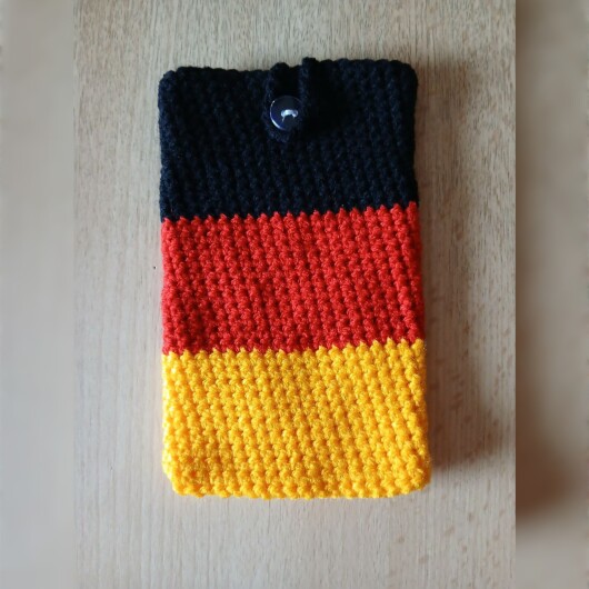 Handgehäkelte Handyhülle klein 10x16 cm in den Farben Schwarz, Rot und Gold, angeordnet wie die deutsche Flagge. Aus robustem Baumwollgarn gefertigt, mit weicher Struktur und sicherem Knopfverschluss oben. Schützt das Smartphone vor Kratzern und Stößen. Ein handgemachtes Accessoire für Fans und Liebhaber deutscher Farben.