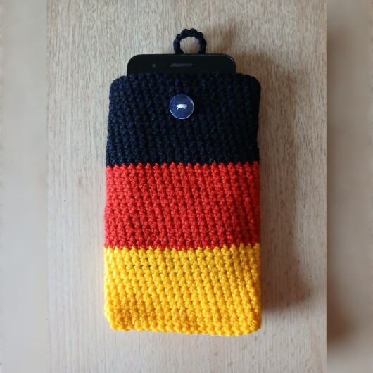 Handgehäkelte Handyhülle klein 10x16 cm in den Farben Schwarz, Rot und Gold, angeordnet wie die deutsche Flagge. Aus robustem Baumwollgarn gefertigt, mit weicher Struktur und sicherem Knopfverschluss oben. Schützt das Smartphone vor Kratzern und Stößen. Ein handgemachtes Accessoire für Fans und Liebhaber deutscher Farben.