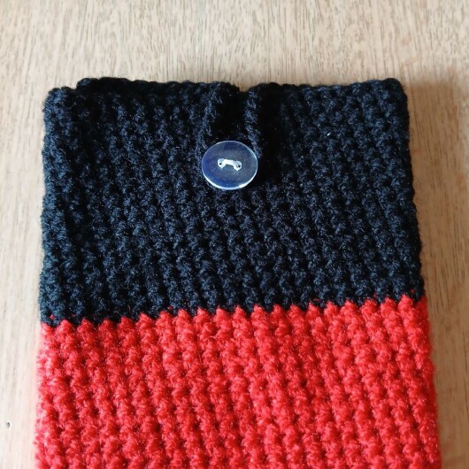 Handgehäkelte Handyhülle klein 10x16 cm in den Farben Schwarz, Rot und Gold, angeordnet wie die deutsche Flagge. Aus robustem Baumwollgarn gefertigt, mit weicher Struktur und sicherem Knopfverschluss oben. Schützt das Smartphone vor Kratzern und Stößen. Ein handgemachtes Accessoire für Fans und Liebhaber deutscher Farben.