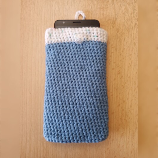 Handgehäkelte zweifarbige Handyhülle Hellblau-Weiß aus weicher, strapazierfähiger Wolle mit dekorativem Knopfverschluss. Die Hülle misst etwa 10 x 16 cm, ist dehnbar und passt sich der Form des Smartphones an. In sanften Pastelltönen gestaltet, schützt sie das Handy vor Kratzern und Stößen – ein stilvolles, handgefertigtes Accessoire mit liebevollen Details.