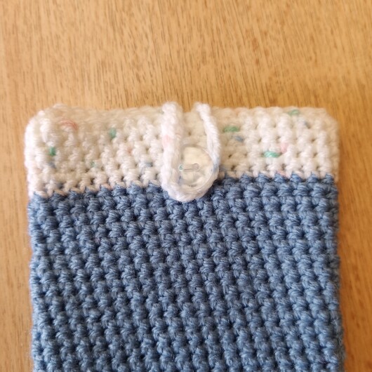 Handgehäkelte zweifarbige Handyhülle Hellblau-Weiß aus weicher, strapazierfähiger Wolle mit dekorativem Knopfverschluss. Die Hülle misst etwa 10 x 16 cm, ist dehnbar und passt sich der Form des Smartphones an. In sanften Pastelltönen gestaltet, schützt sie das Handy vor Kratzern und Stößen – ein stilvolles, handgefertigtes Accessoire mit liebevollen Details.