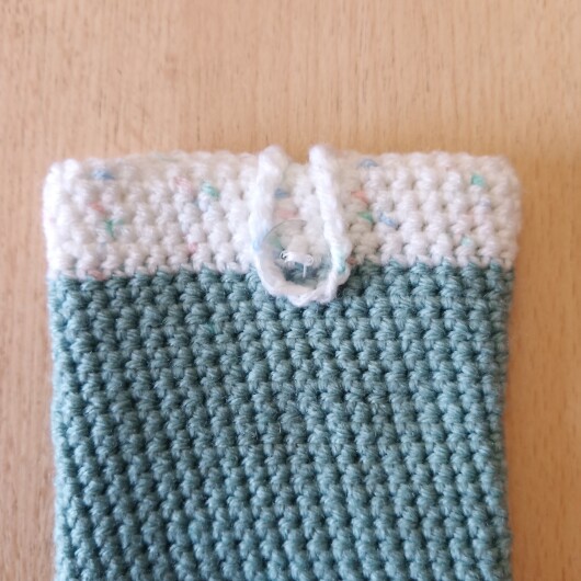Handgehäkelte zweifarbige Handyhülle Mintgrün-Weiß aus weicher, strapazierfähiger Wolle mit dekorativem Knopfverschluss. Die Hülle misst etwa 10 x 16 cm, ist dehnbar und passt sich der Form des Smartphones an. In sanften Pastelltönen gestaltet, schützt sie das Handy vor Kratzern und Stößen – ein stilvolles, handgefertigtes Accessoire mit liebevollen Details.