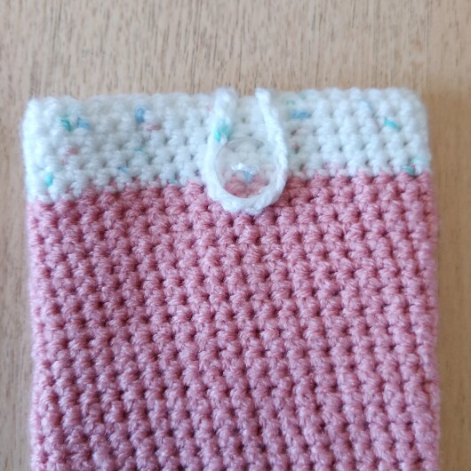 Handgehäkelte zweifarbige Handyhülle Rosa-Weiß aus weicher, strapazierfähiger Wolle mit dekorativem Knopfverschluss. Die Hülle misst etwa 10 x 16 cm, ist dehnbar und passt sich der Form des Smartphones an. In sanften Pastelltönen gestaltet, schützt sie das Handy vor Kratzern und Stößen – ein stilvolles, handgefertigtes Accessoire mit liebevollen Details.
