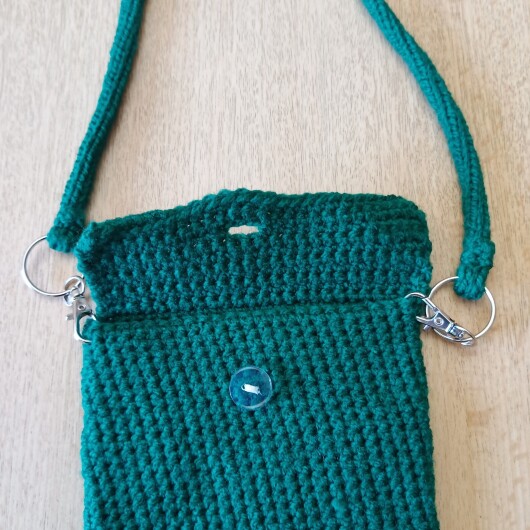 Handgehäkelte Handytasche Dunkelgrün aus hochwertigem Garn mit gleichmäßiger Struktur und Knopfverschluss. Die Tasche misst etwa 12 x 20 cm, bietet Platz für ein Smartphone und kleine Alltagsgegenstände. Mit abnehmbarem Schultergurt, der wahlweise als Umhängetasche oder Handyhülle genutzt werden kann. In verschiedenen Farben erhältlich – ein handgemachtes, stilvolles und nachhaltiges Accessoire.