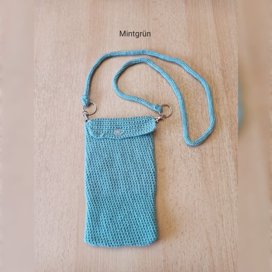 Handgehäkelte Handytasche Mintgrün aus hochwertigem Garn mit gleichmäßiger Struktur und Knopfverschluss. Die Tasche misst etwa 12 x 20 cm, bietet Platz für ein Smartphone und kleine Alltagsgegenstände. Mit abnehmbarem Schultergurt, der wahlweise als Umhängetasche oder Handyhülle genutzt werden kann. In verschiedenen Farben erhältlich – ein handgemachtes, stilvolles und nachhaltiges Accessoire.