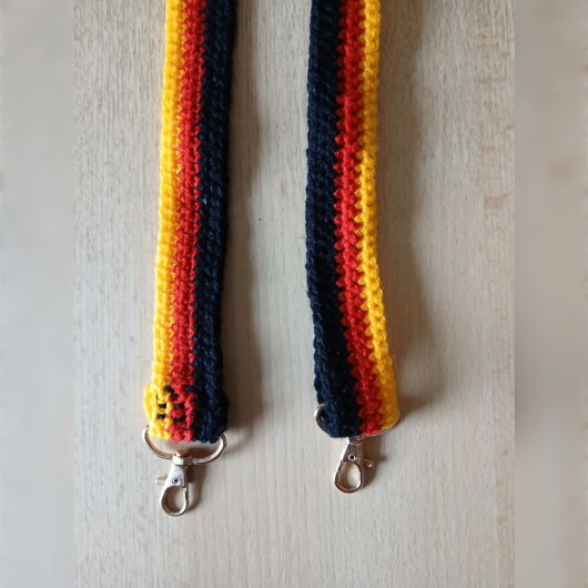 Handgehäkelte Umhängetasche in den Farben Schwarz, Rot und Gold, inspiriert von der deutschen Flagge. Mit breitem, verstellbarem Schultergurt, stabilem Kordelzugverschluss und dekorativem Kordelende. Etwa 19 x 26 cm groß, bietet Platz für Alltagsutensilien wie Handy, Geldbörse und Schlüssel. Stilvolles, handgemachtes Accessoire für Fans und Liebhaber deutscher Farben.