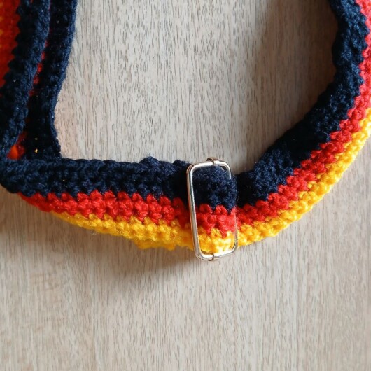 Handgehäkelte Umhängetasche in den Farben Schwarz, Rot und Gold, inspiriert von der deutschen Flagge. Mit breitem, verstellbarem Schultergurt, stabilem Kordelzugverschluss und dekorativem Kordelende. Etwa 19 x 26 cm groß, bietet Platz für Alltagsutensilien wie Handy, Geldbörse und Schlüssel. Stilvolles, handgemachtes Accessoire für Fans und Liebhaber deutscher Farben.