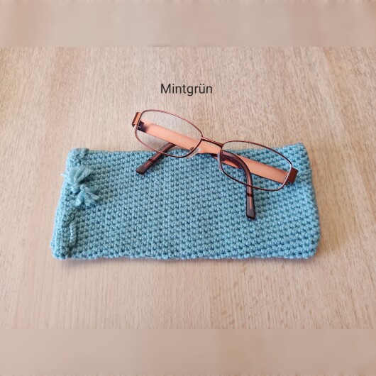Handgehäkeltes Brillenetui Mintgrün aus weicher Baumwolle mit handgeflochtenem Kordelzug. Das etwa 9 x 20 cm große Etui bietet Platz für Lese-, Sonnen- oder Sehbrillen und schützt sie zuverlässig vor Kratzern und leichten Stößen. Leichtes, schlankes Design mit rustikalem Charme – in verschiedenen Farben erhältlich, handgefertigt und nachhaltig hergestellt.
