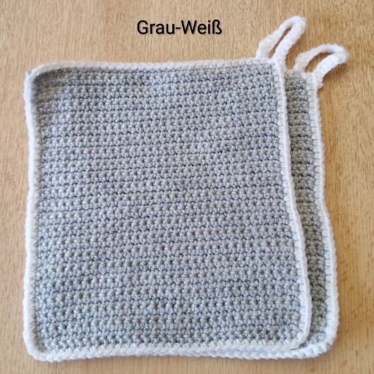 Handgehäkeltes Topflappen-Set Grau-Weiß aus robustem Baumwollgarn, quadratisch mit ca. 16 x 16 cm Größe. Die gleichmäßige Häkelstruktur sorgt für Hitzeschutz beim Kochen und Backen. Jeder Topflappen hat eine stabile Aufhängeschlaufe und ist wahlweise einfarbig oder mit farbigem Rand gestaltet – ein dekorativer, funktionaler Küchenhelfer in Handarbeit.