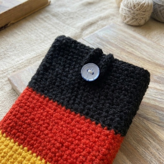 Handgehäkelte Handyhülle Deutschland Handyhülle in den Farben Schwarz, Rot und Gold, angeordnet wie die deutsche Flagge. Aus robustem Wollgarn gefertigt, mit weicher Struktur und sicherem Knopfverschluss oben. Schützt das Smartphone vor Kratzern und Stößen. Erhältlich in zwei Größen – ein handgemachtes Accessoire für Fans und Liebhaber deutscher Farben.