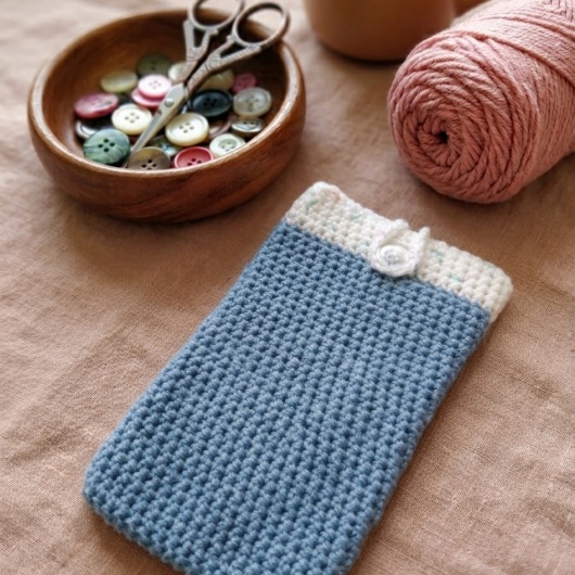 Handgehäkelte Handyhülle Zweifarbige Handyhülle aus weicher, strapazierfähiger Wolle mit dekorativem Knopfverschluss. Die Hülle misst etwa 10 x 16 cm, ist dehnbar und passt sich der Form des Smartphones an. In sanften Pastelltönen gestaltet, schützt sie das Handy vor Kratzern und Stößen – ein stilvolles, handgefertigtes Accessoire mit liebevollen Details.
