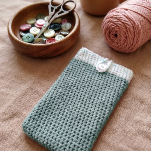 Handgehäkelte Handyhülle Zweifarbige Handyhülle aus weicher, strapazierfähiger Wolle mit dekorativem Knopfverschluss. Die Hülle misst etwa 10 x 16 cm, ist dehnbar und passt sich der Form des Smartphones an. In sanften Pastelltönen gestaltet, schützt sie das Handy vor Kratzern und Stößen – ein stilvolles, handgefertigtes Accessoire mit liebevollen Details.