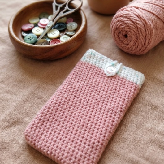 Handgehäkelte Handyhülle Zweifarbige Handyhülle aus weicher, strapazierfähiger Wolle mit dekorativem Knopfverschluss. Die Hülle misst etwa 10 x 16 cm, ist dehnbar und passt sich der Form des Smartphones an. In sanften Pastelltönen gestaltet, schützt sie das Handy vor Kratzern und Stößen – ein stilvolles, handgefertigtes Accessoire mit liebevollen Details.