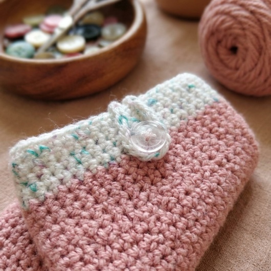 Handgehäkelte Handyhülle Zweifarbige Handyhülle aus weicher, strapazierfähiger Wolle mit dekorativem Knopfverschluss. Die Hülle misst etwa 10 x 16 cm, ist dehnbar und passt sich der Form des Smartphones an. In sanften Pastelltönen gestaltet, schützt sie das Handy vor Kratzern und Stößen – ein stilvolles, handgefertigtes Accessoire mit liebevollen Details.