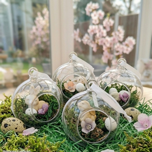 Handgefertigte Osterkugel Handgemachter Osterschmuck aus Acryl mit einer Miniaturszene im Inneren: ein kleiner Osterhase sitzt auf einem Bett aus grünem Moos, daneben ein zartes Deko-Ei und feine Blüten. Die Kugel hängt an einem weißen Satinband und wirkt natürlich, frühlingshaft und elegant – ein stilvoller Osterschmuck zum Aufhängen oder Verschenken.