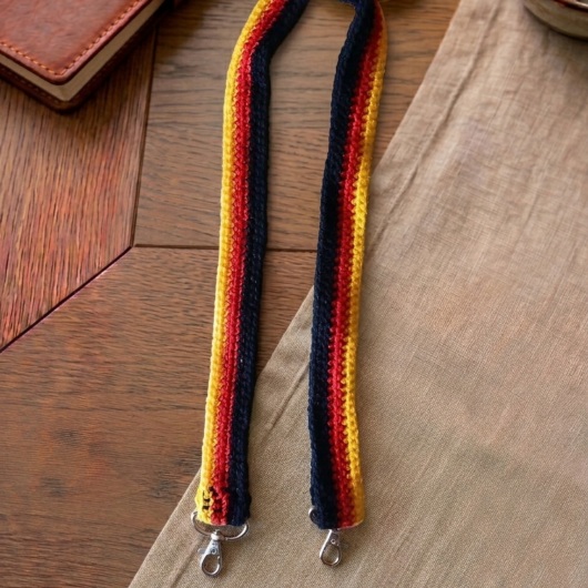 Handgehäkelte Tasche Deutschland Tasche in den Farben Schwarz, Rot und Gold, inspiriert von der deutschen Flagge. Mit breitem, verstellbarem Schultergurt, stabilem Kordelzugverschluss und dekorativem Kordelende. Etwa 19 x 26 cm groß, bietet Platz für Alltagsutensilien wie Handy, Geldbörse und Schlüssel. Stilvolles, handgemachtes Accessoire für Fans und Liebhaber deutscher Farben.